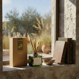 SAUSSAVITA Wild Citrus diffuser in green glass with reeds, beside citrus box on rustic window sill with natural light